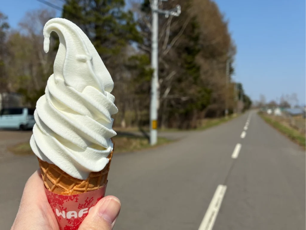 恵庭のミルク小屋で購入したワッフルコーンのソフトクリーム。店舗前の道路から車で訪れる立地の雰囲気が分かる写真。