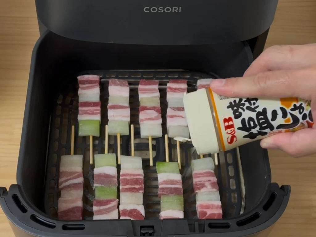 COSORIに並べた豚ばらねぎ間串10本に塩こしょうで味付けしている様子