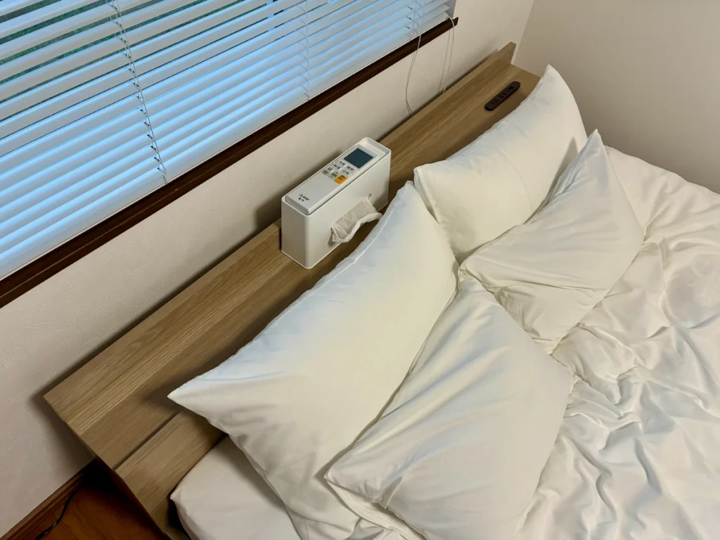 Yoichi Niki Retreatのベッドに置かれた2種類の枕と、ティッシュ・コンセント・USBポートを備えたヘッドボード