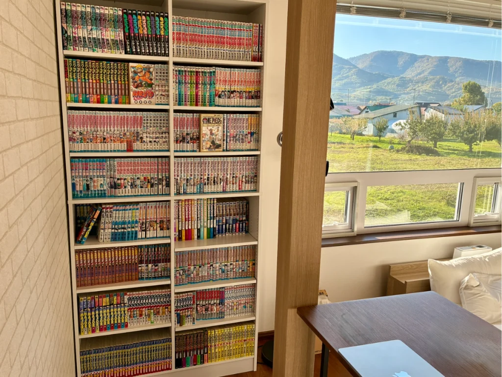 Yoichi Niki Retreatの2階にある漫画本棚と、窓から望む仁木町の山並み